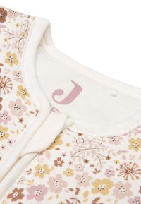 Vêtement en coton à motif floral avec un fond crème, présentant de petites fleurs jaunes, roses et marron. Comprend un col rond et un détail de bouton.