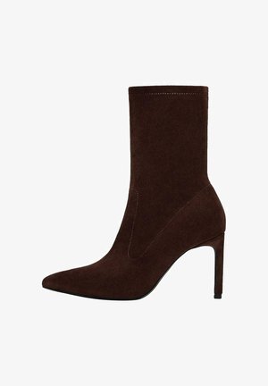 Stivaletto alla caviglia in suede marrone con punta appuntita e tacco a spillo alto. Presenta una tomaia senza cuciture e dettagli di cuciture sottili.