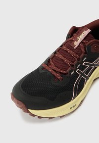 Black athletic shoe with maroon accents. Features a mesh upper, rubber sole, and light-colored cushioning. Notable logo on the side.