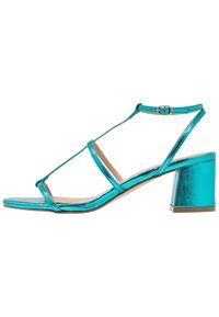 Vihreät metallinhohtoiset korkokengät, joissa on T-nauha-muotoilu, ohuet hihnat ja paksu korko. Liukas pinta kiiltävällä viimeistelyllä.