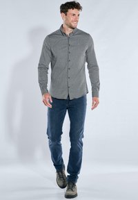 Hellgraues Hemd mit Muster, dunkelblaue Jeans und graue Stiefel. Das Hemd hat einen kleinen geometrischen Druck und lange Ärmel.