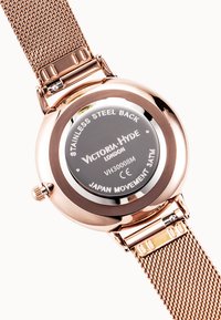 Orologio rotondo con retro in acciaio inossidabile. Cinturino a maglia color oro rosa. Il quadrante nero presenta il nome del marchio e i dettagli del movimento incisi.
