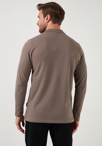 Camisa de manga larga en marrón claro, hecha de una tela suave. Presenta un cuello clásico y un corte recto con una sutil textura.