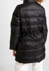 Zwarte gewatteerde jas met een hoge kraag, voorzien van horizontale quilting en een getailleerde taille. Gemaakt van glanzend, lichtgewicht materiaal.