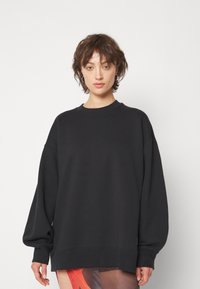Sudadera negra de gran tamaño con escote redondo, mangas largas y amplias, y textura suave. La línea del dobladillo se extiende más allá de la cintura para un ajuste relajado.