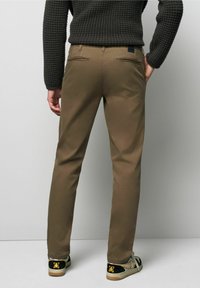 Bruine katoenen chinos met een slim fit, voorzien van achterzakken en een zwart logo-opdruk. Gepaarde met multikleurige sneakers.