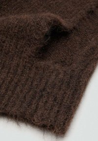 Bruin gebreide stof met een zachte, pluizige textuur. Heeft geribbelde details langs de rand, die de diepte en warmte van het materiaal benadrukken.