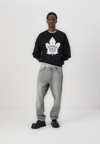 Hanorac negru cu grafica albă "Toronto Maple Leafs", asortat cu blugi gri deschis și pantofi masivi negri. Design simplu cu o croială lejeră.
