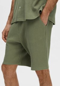 Gröna shorts med våfflat mönster och sidofickor, designade för komfort. Löst snitt med knälång längd och sydd nedre kant.