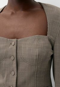 Hnědý kostkovaný krátký top se čtvercovým výstřihem, s texturovaným povrchem a dvěma ozdobnými knoflíky na přední straně.