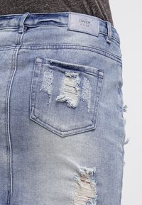 Ljusblå slitna denimshorts med ett trasigt fickdetalj, fransade kanter och en märkespatch vid bakre midjan.