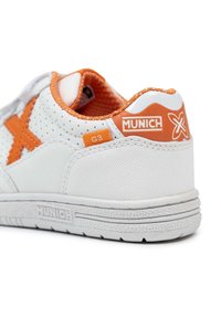 Zapatilla blanca con acentos en naranja y textura perforada. Presenta una suela texturizada, detalle del logo y un collar acolchado para mayor comodidad.
