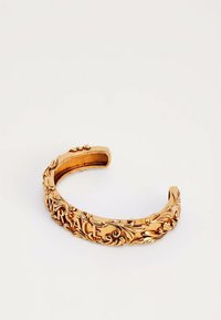 Brazalete abierto de tono dorado con patrones florales ornamentales de estilo barroco y nombre de la marca "VERSACE" parcialmente visible grabado.