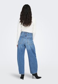 Höga, löst sittande blå denimjeans med två bakfickor och en blekt textur, kombinerade med en ribbad vit långärmad topp och svarta klackskor.