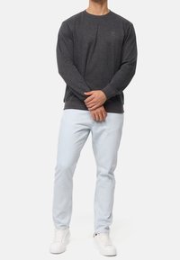 Felpa grigia scura con collo rotondo e polsini a coste, abbinata a jeans in denim azzurri e sneakers bianche. Outfit semplice e casual.