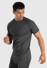 Donkergrijze sport-t-shirt met korte mouwen. Glad, rekbaar materiaal met een ronde halslijn en subtiele zijnaad. Model in actie geposeerd.