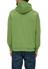 Sudadera verde con una textura suave, que presenta una capucha con cordones y puños de canalé. Combinada con unos vaqueros de color azul oscuro, mostrando un ajuste casual.