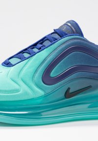Sneaker Nike Air Max z gradientowym turkusowym wierzchem, niebieskimi sznurowadłami i przezroczystą podeszwą powietrzną. Czarny akcent z logotypem po boku.