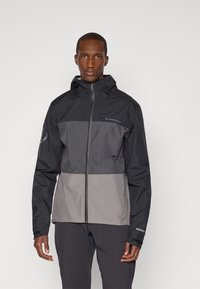 Veste étanche en coloris noir et gris avec capuche, fermeture éclair et logo sur la poitrine, présentant une coupe structurée et des poignets élastiques.