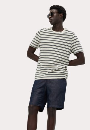 Camiseta de cuello redondo a rayas en color crema, con líneas azul oscuro, combinada con pantalones cortos de mezclilla oscuros. Modelo lleva gafas de sol negras.