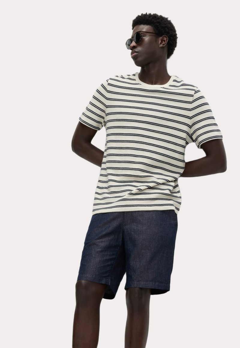 Randig crew neck t-shirt i krämvit, med mörkblå ränder, tillsammans med mörka denimshorts. Modell bär svarta solglasögon.