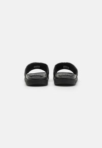 Black slide sandals with a textured rubber footbed, open back design, and a smooth finish. Lightweight and designed for comfort.