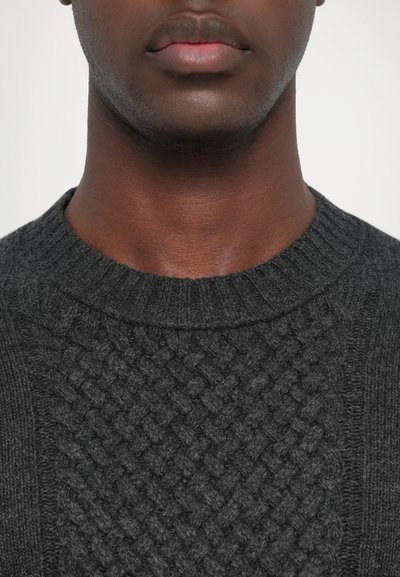 Un pull tricoté gris foncé avec un motif tissé texturé à l'avant et un col rond côtelé. Matériau doux de poids moyen.