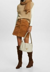 Maglione a coste color tan, gonna in velluto a coste marrone, stivali al ginocchio in suede marrone e una borsa beige con chiusura a scatto e forma strutturata.