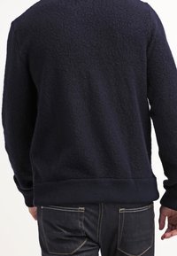 Marinblå tröja i fleece med textur, med ribbad nederdel och ärmar, i avslappnad passform, bärs över mörka jeans.