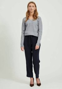 Suéter gris de cuello en V combinado con pantalones de chándal azul marino. La ropa presenta puños acanalados y un corte relajado. El modelo lleva tacones de print de leopardo marrón.