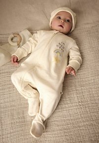 Krémové detské body s predným zipsom, s potlačeným textom, dúhou a dizajnom hviezdy. V balení s ňou je aj zodpovedajúca čiapka a drevený hryzátko.