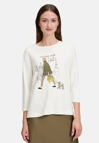 Weißes Langarm-T-Shirt mit einer illustrierten Szene einer Frau, die einen Hund spazieren führt, mit grünem Mantel und gelber Tasche.