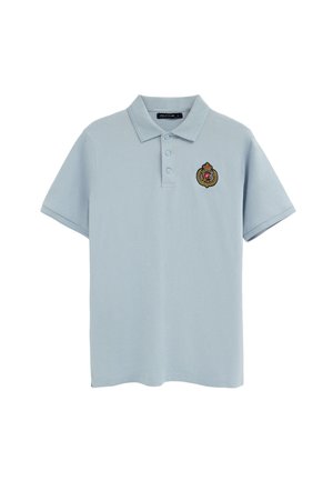 Hellblaues Poloshirt mit kurzen Ärmeln, drei Knöpfen und einem kleinen bestickten Wappen mit Krone und "P" auf der linken Brust.
