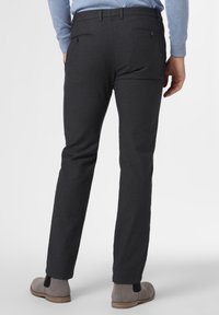 Pantaloni grigio scuro in tessuto testurizzato, con tasche posteriori con bottoni e vestibilità slim, abbinati a scarpe grigio chiaro.