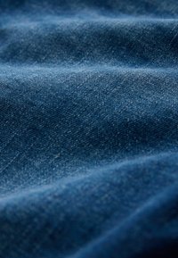 Nærbillede af blåt denimstof med tekstur, der viser vævemønster og subtile folder.