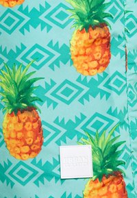 Tissu à motif d'ananas en turquoise, avec des ananas orange vif et verts. Comprend une étiquette blanche "URBAN CLASSICS".