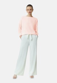 Lichtroze trui met een brede halslijn en lange mouwen, gecombineerd met lichtblauwe wijduitlopende broek met een gestrikte tailleband. Witte sandaaltjes maken de look af.
