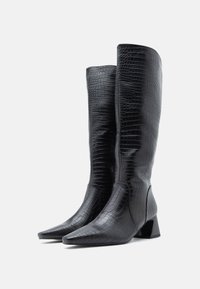 Bottes noires montantes jusqu'au genou en cuir embossé crocodile, avec un bout pointu et un talon bloc. Texture lisse, design épuré.