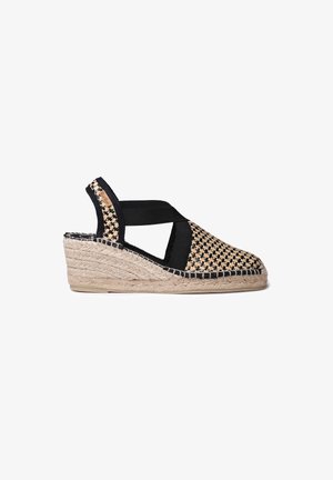 Compensée espadrille tissée avec des sangles élastiques noires. Dessus de couleur paille naturelle avec un motif texturé et semelle en jute tressé.