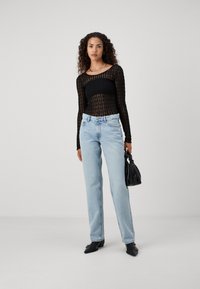 Svart gjennomsiktig langermet topp med teksturert mønster, kombinert med lyseblå rette jeans og svarte spisse sko; holder en liten svart veske.