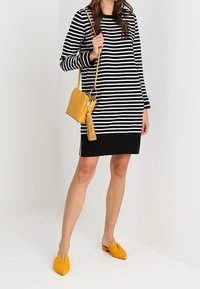 Vestido de rayas blancas y negras de manga larga, de longitud por encima de la rodilla, combinado con un pequeño bolso amarillo cruzado y mocasines amarillos.