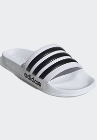 Adidas sandaler med hvit base, tre svarte teksturerte striper på overdelen og en gummisåle. Har 'adidas'-logotrykk på siden.