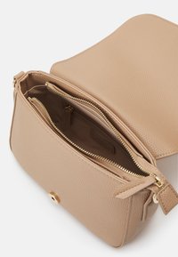 Borsa a mano in pelle beige con superficie texturizzata, hardware dorato, chiusura con zip superiore e scomparti interni per l'organizzazione.