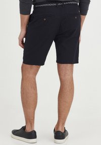 Men's dark navy shorts with a smooth cotton blend, featuring back pockets and wear-resistant stitching, paired with black sneakers.