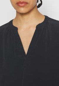 Sort, lette bluse med v-hals, blød tekstur og subtile plisseringer ved skuldrene. Har et minimalistisk design.