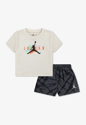 T-shirt Jordan de couleur crème avec un logo noir, orange et turquoise, associée à un short noir à motifs avec un petit logo Jumpman blanc.