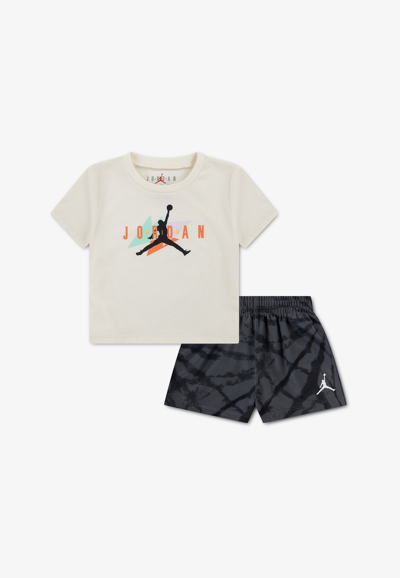 T-shirt Jordan de couleur crème avec un logo noir, orange et turquoise, associée à un short noir à motifs avec un petit logo Jumpman blanc.