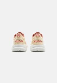 Beige and pink sneaker with white outsole, featuring "HUGO" logo on the heel, textured material, and padded collar for comfort.