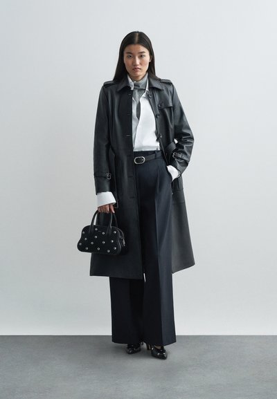 Black leather long coat with button details, white shirt, gray scarf, tailored navy trousers, and a small black handbag with rivets.