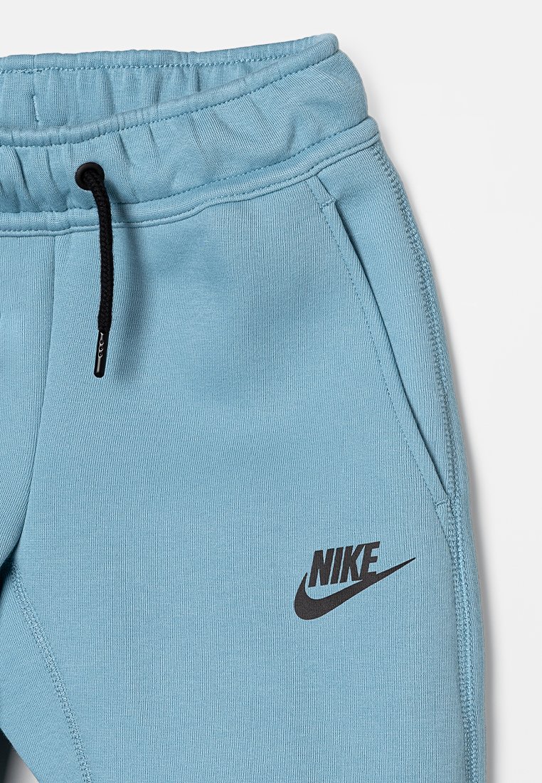 Jasnoniebieskie spodnie dresowe Nike z elastycznym pasem, czarnym sznurkiem do ściągania i logo. Gładka tkanina z bocznymi kieszeniami i zwężającymi się nogawkami.